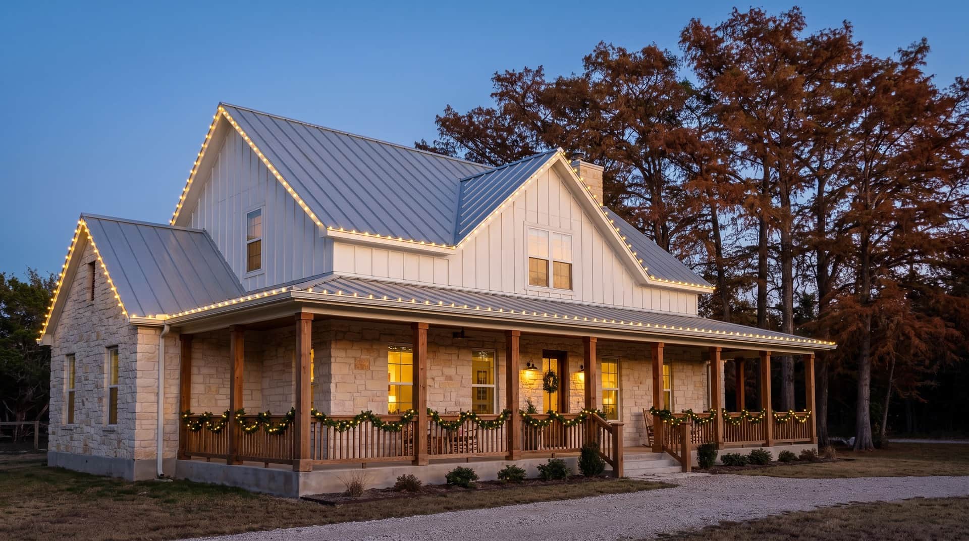 Design mockup: a Texas German farmhouse-style home in New Braunfels with limestone lower walls, white board and batten, a metal roof and a deep front porch, bald cypress trees behind, at dusk with warm white roofline lights and lit garland on the porch rail