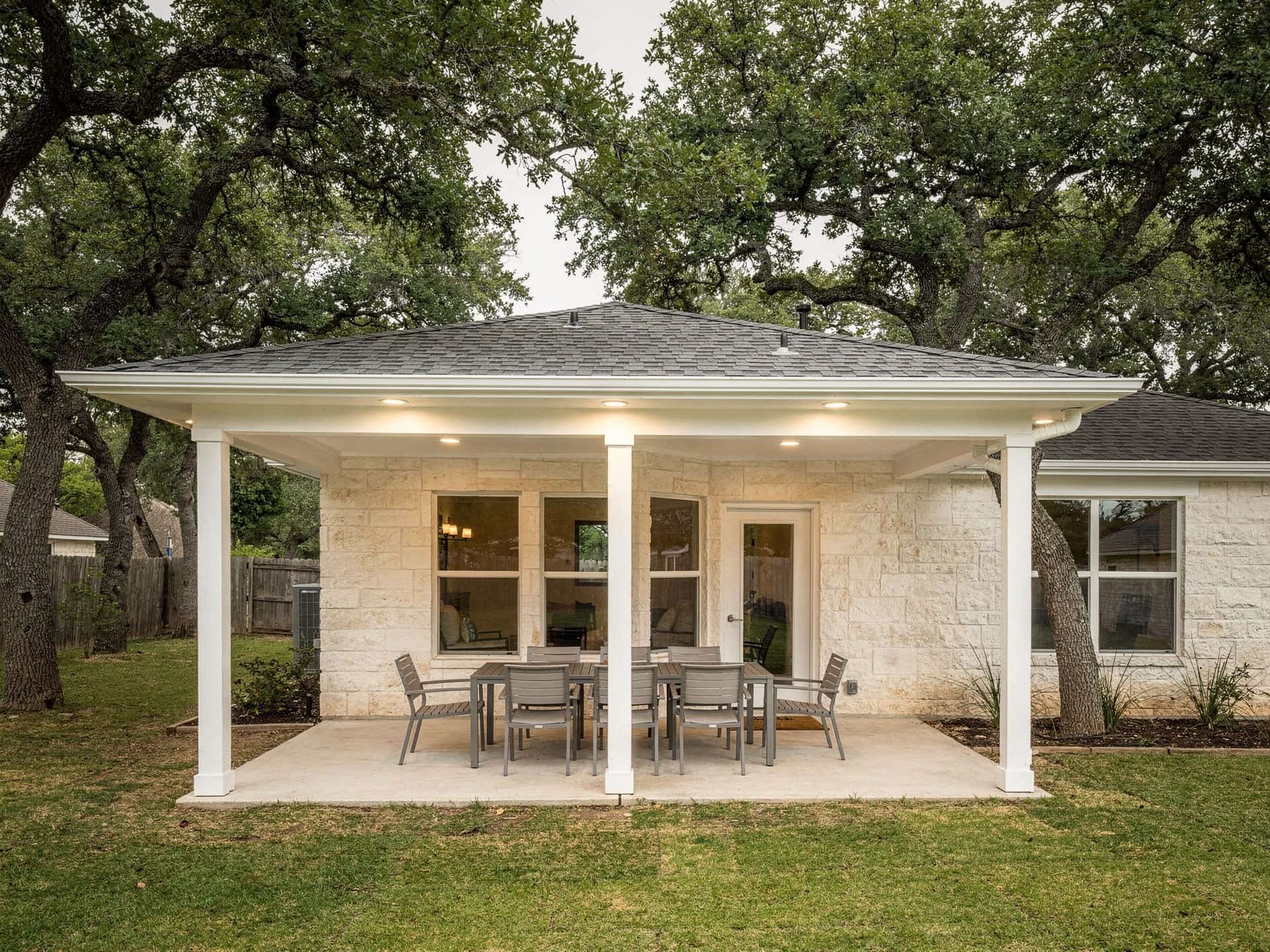 Attached shingle patio cover with white posts and recessed lights over a dining patio