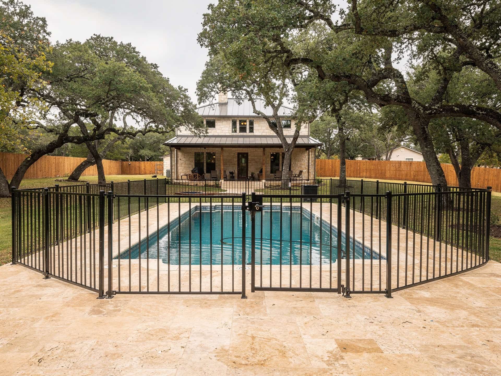 Black wrought iron pool fence with a self-closing gate around a travertine pool deck