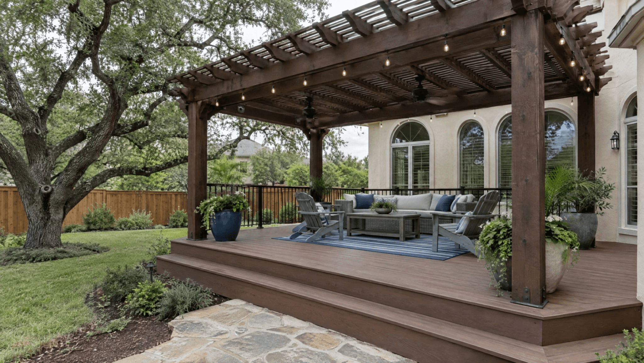 Stained cedar pergola with ceiling fans and string lights on a raised composite deck with wide steps behind a stucco home in San Antonio