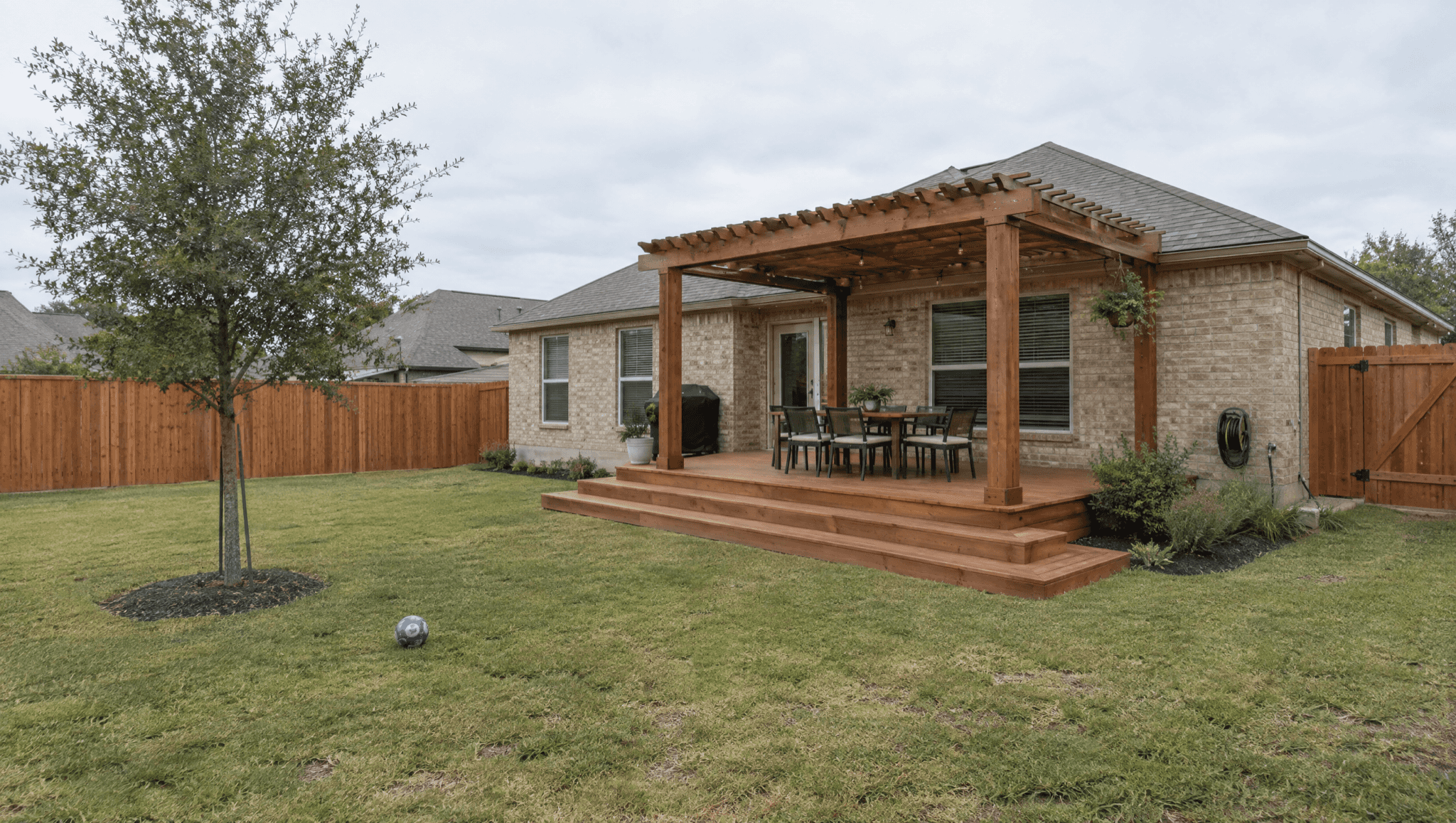Ground-level wood deck with wide steps and a pergola on a lawn