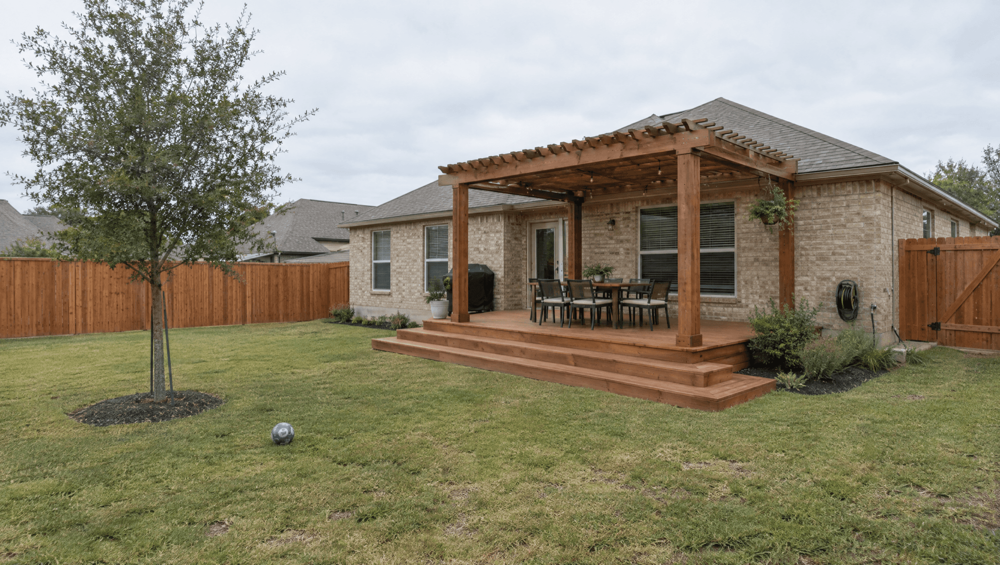 Low cedar deck with wide steps and a cedar pergola behind a single-story brick home in San Antonio
