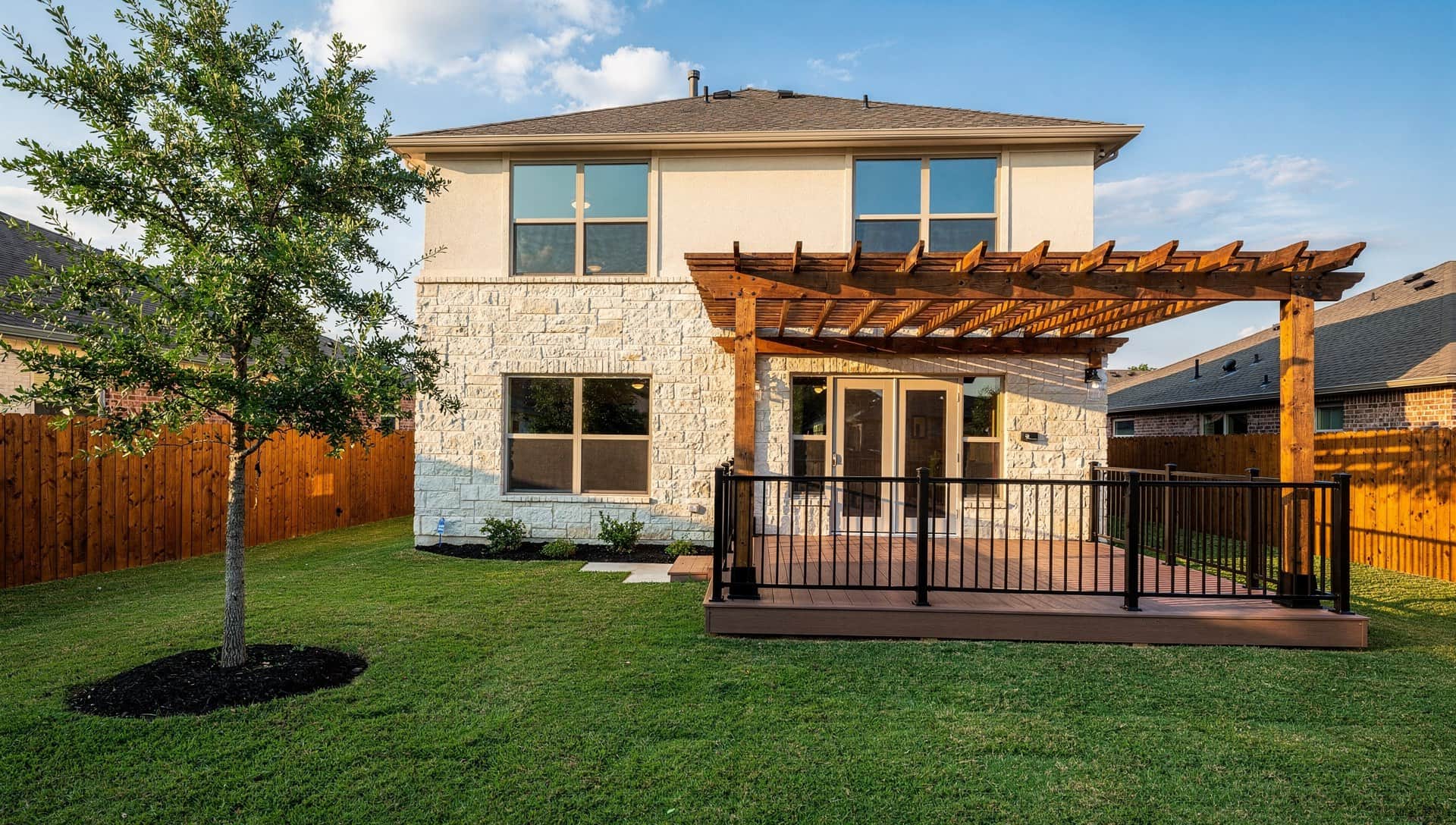 Composite deck with black railing under a cedar pergola behind a two-story limestone home in San Antonio
