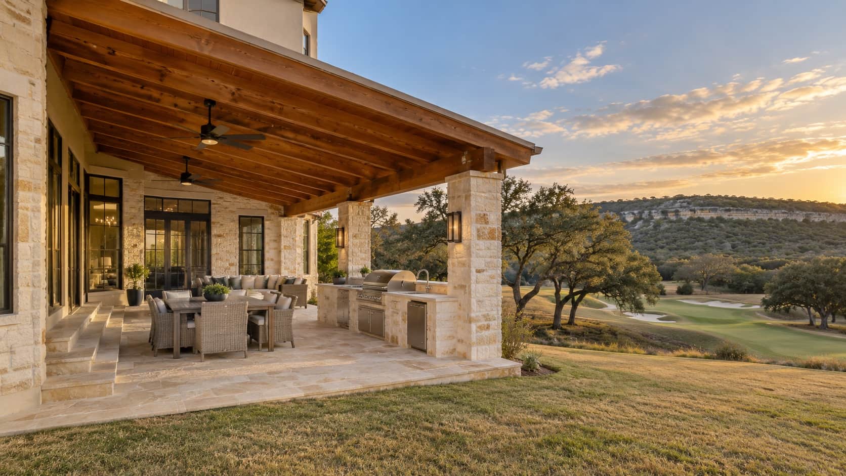 Covered patio with a cedar shed roof, ceiling fans and a limestone outdoor kitchen looking out on a golf fairway and live oaks, the kind Klema builds in Canyon Springs