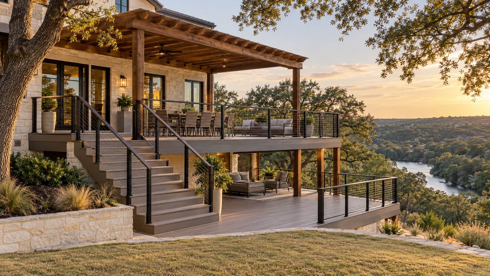 Two-level composite deck with cable railing and a cedar pergola on a limestone Hill Country home above a wooded river valley, the kind Klema builds in Cordillera Ranch