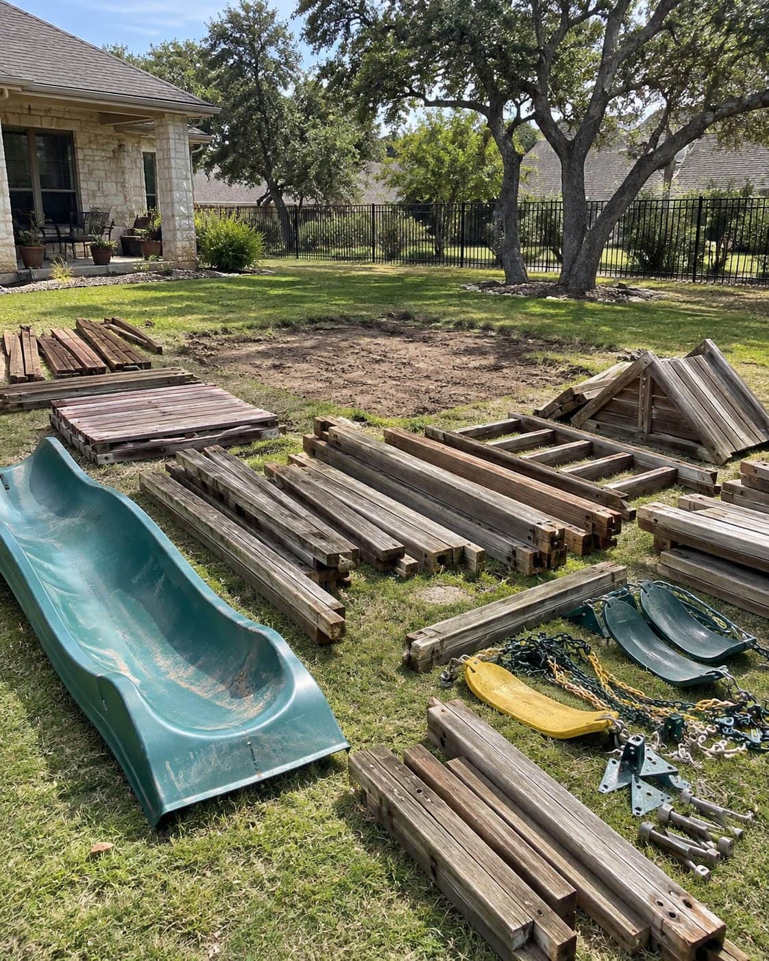 Old wooden swing set taken apart on the lawn, beams, slide and swings in piles beside the bare patch where it stood