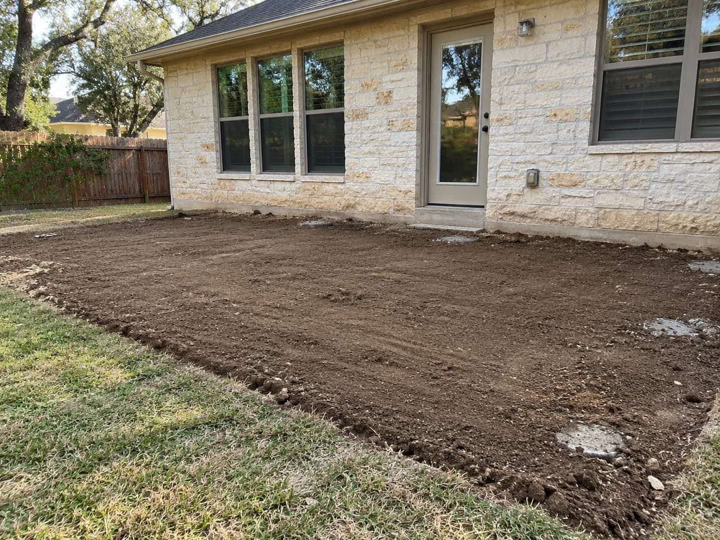 Backyard graded and raked smooth after a removal, house wall behind and no debris left