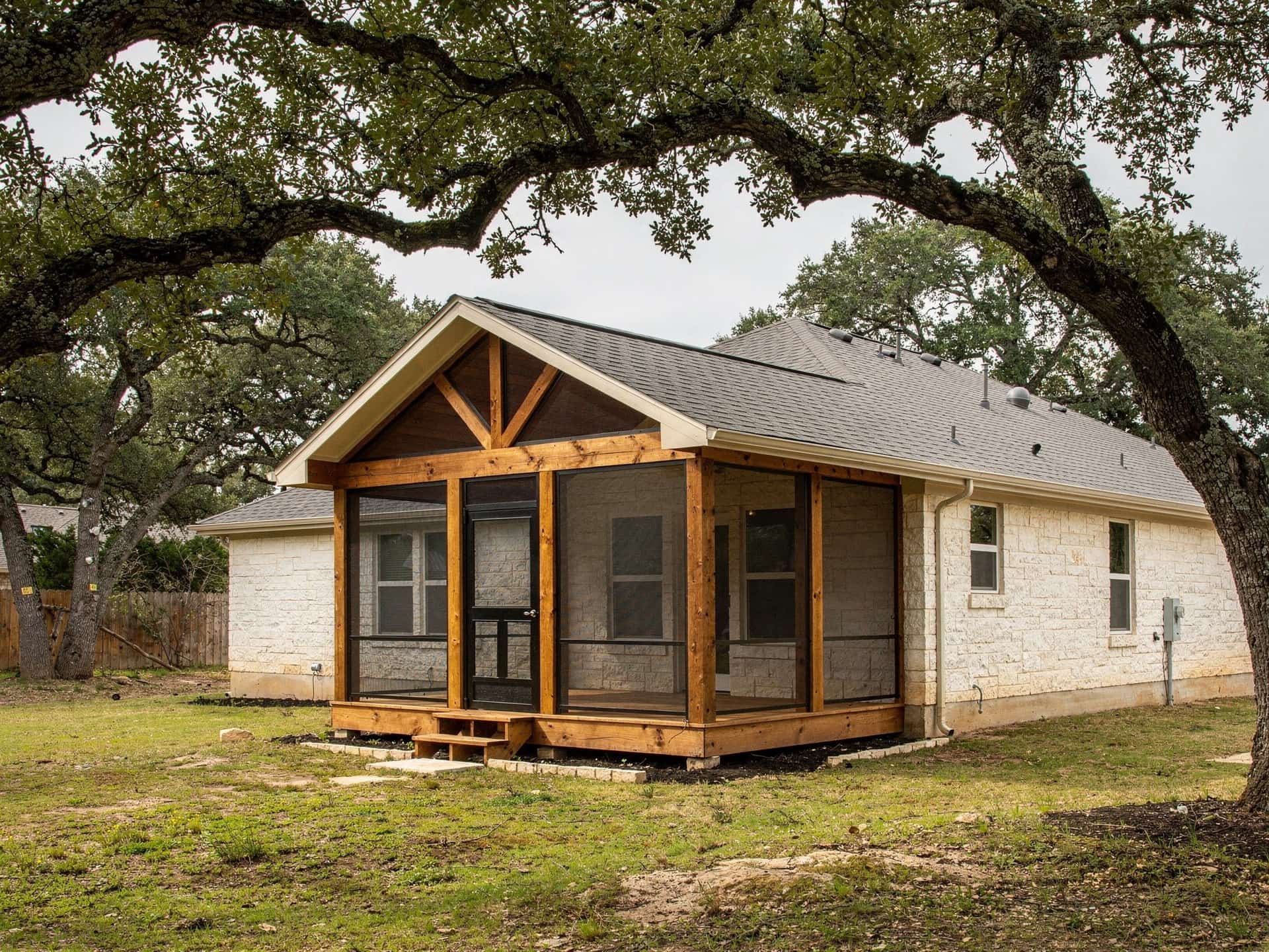 New screened porch addition with a gable shingle roof and cedar posts on a limestone home