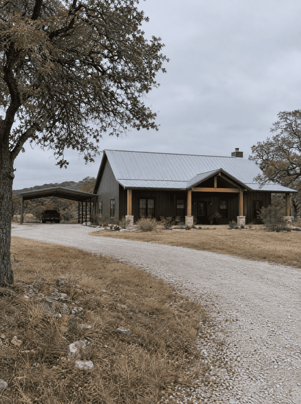 Finished barndominium with a metal roof under live oaks