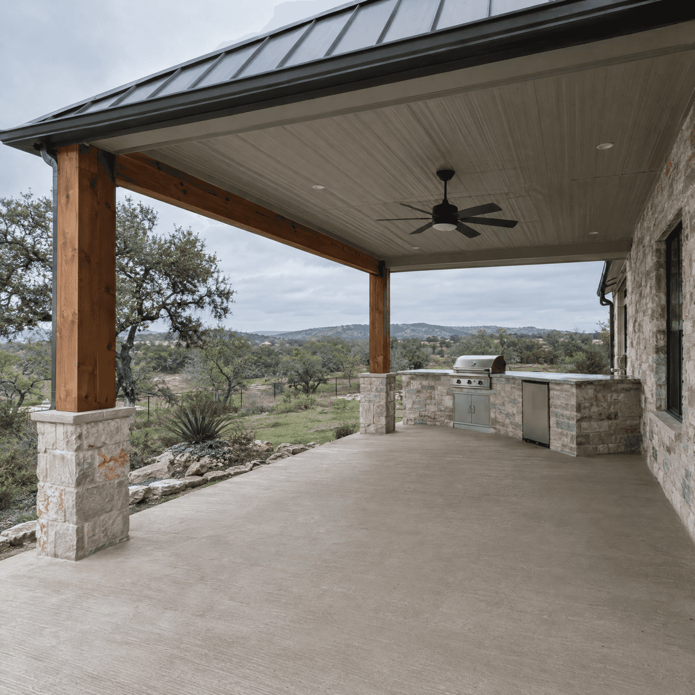 Standing-seam metal patio cover with cedar posts over an outdoor kitchen with a Hill Country view